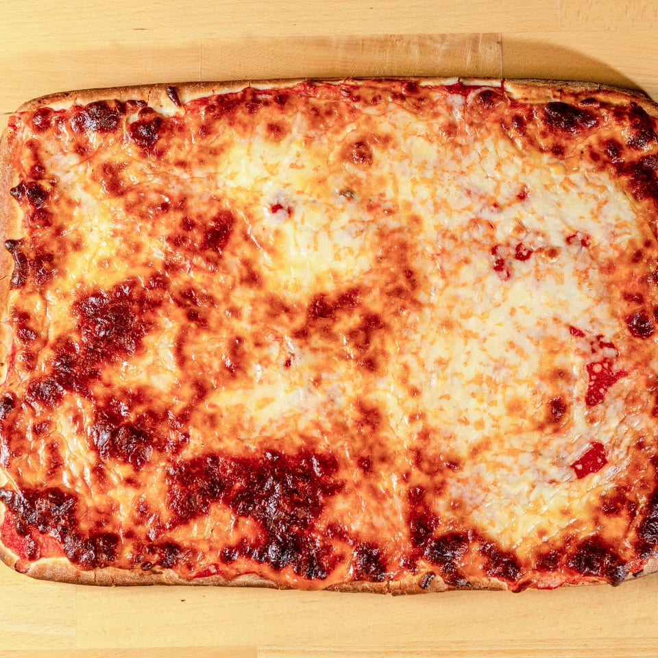 A rectangular cheese pizza from La Pizzeria, with melted golden cheese and red sauce, on a wooden surface.