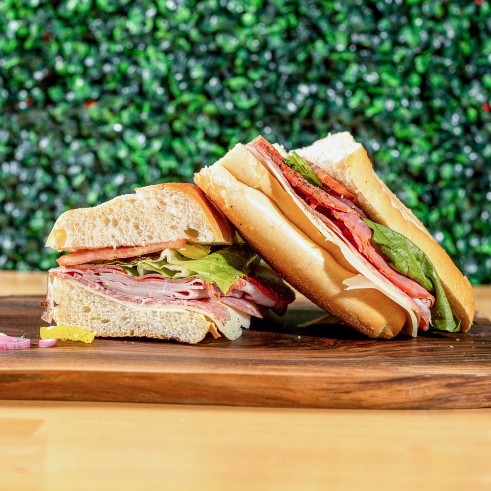 Two halves of a large Italian sub sandwich with various meats, cheese, lettuce, and tomato.