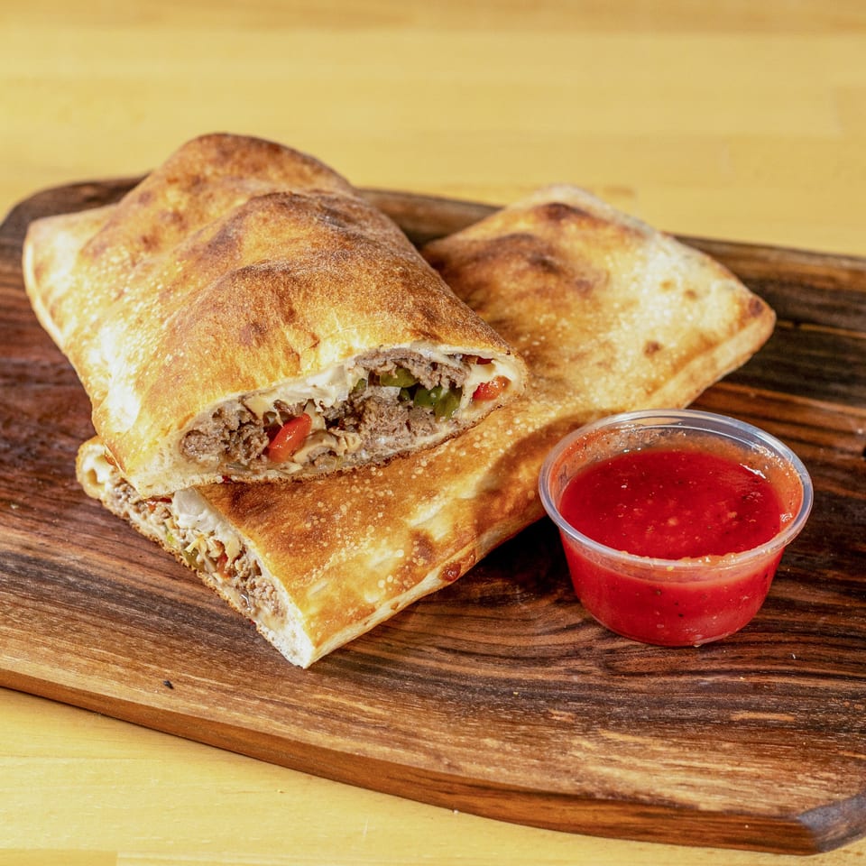 Two La Pizzeria calzones, one sliced open to show meat and vegetables, with a side of marinara sauce.