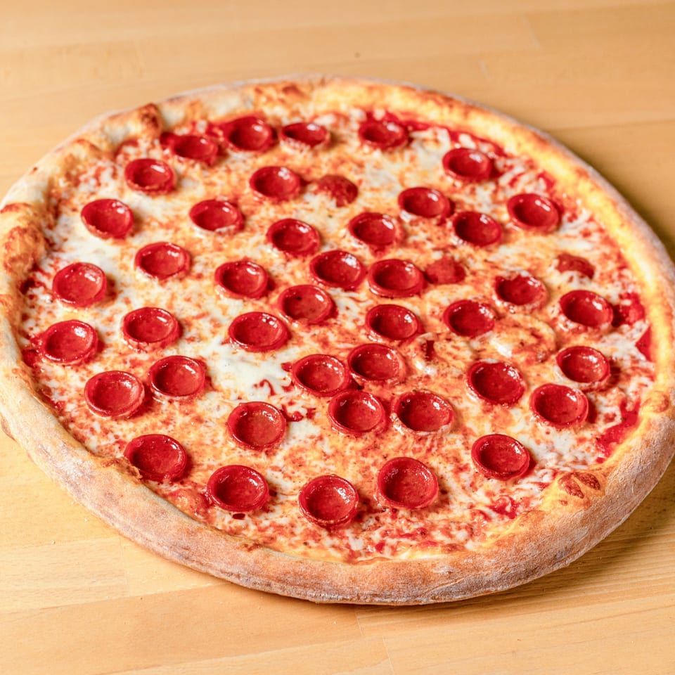 A whole pepperoni pizza from La Pizzeria, with melted cheese and a golden crust, on a wooden table.
