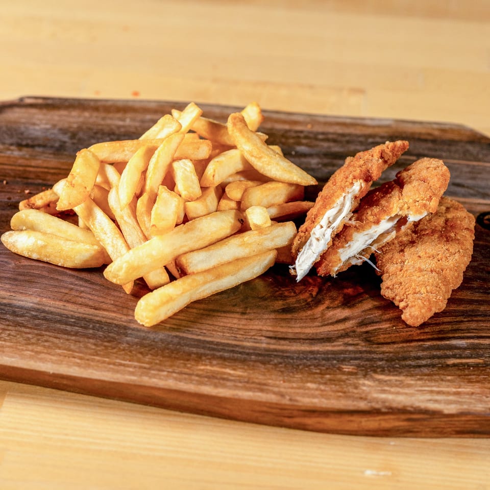 Golden french fries and crispy chicken tenders, one split open, on a rustic wooden board.